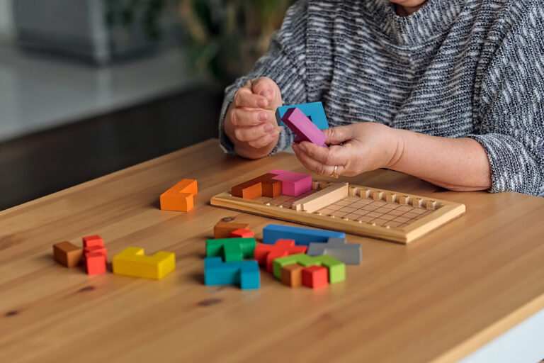 ctivity can improve brain function. Elderly woman sitting at table and sorting jigsaw puzzle pieces, free space game