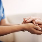 Close-up of a compassionate caregiver in blue scrubs holding an elderly person's hands to offer comfort and support."